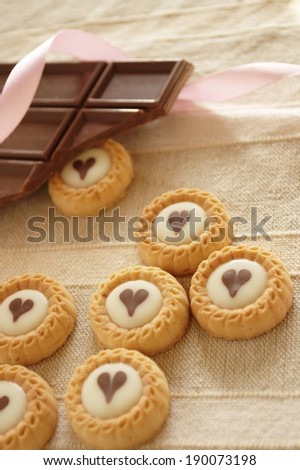 Cookies with white centers and chocolate hearts and a broken chocolate bar with a pink ribbon.