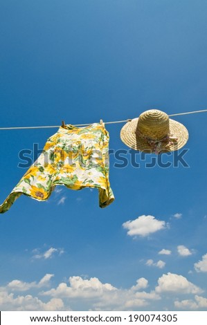 A sun hat and dress hanging from a clothes line on a sunny day.