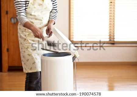 A person emptying a dustpan into a foot-operated trash can.