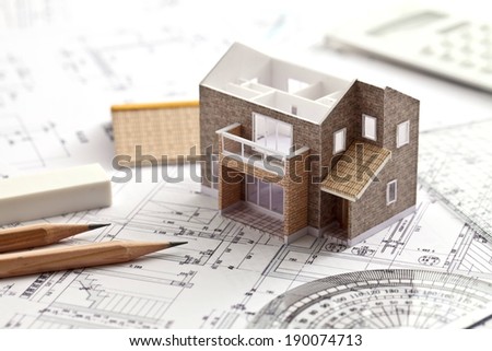 A small house and pencils on a set of blueprints.