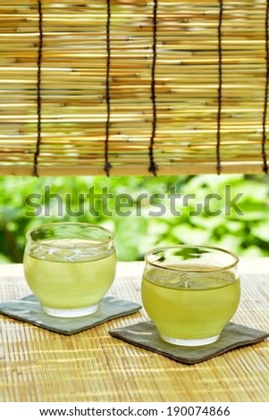 Two filled glasses of pale green liquid on coasters sitting on a straw mat.