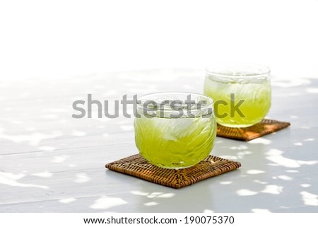 Two glasses of a lime colored drink are each on a coaster.