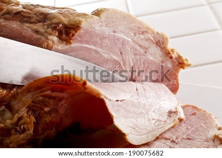 A silver knife cuts thin slices from a slab of pink meat.
