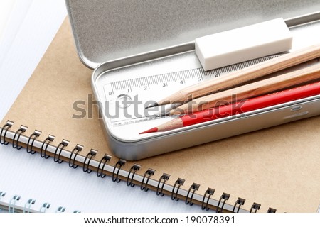 A metal case holding three pencils, one being red.