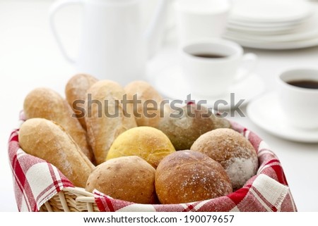 A basket of varied buns and two cups of coffee.