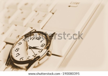 A pocket watch sits on top of a computer keyboard.