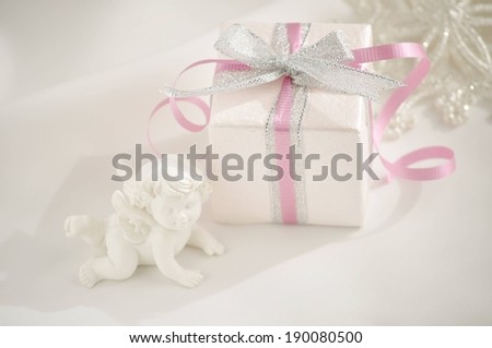 A box wrapped in white paper with pink and white ribbon and bows and an angel