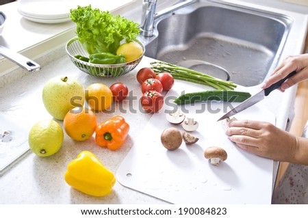 A person cutting up fresh mushrooms, with other vegetables near.