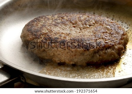 A beef burger patty frying in a pan.