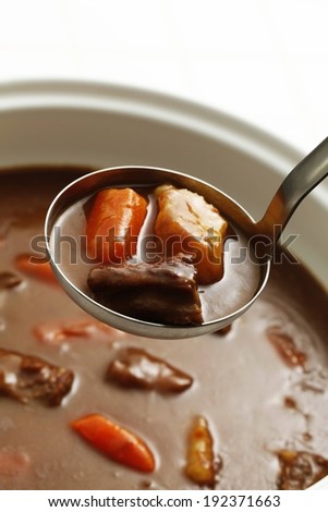 A ladle picks up three pieces of food from a bowl mixture.