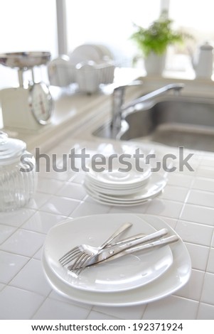 Dishes and cutlery rest on a white tiled kitchen counter in front of a sink.
