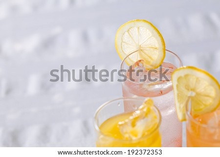 Three beverages in glasses filled with ice with slices of fruit.