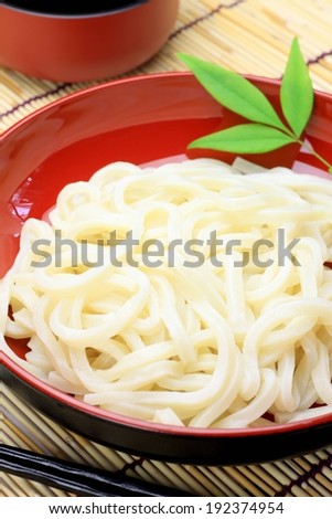 A red bowl full of noodles and a red pot next to it.