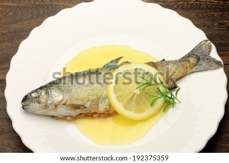 A cooked fish on a plate with a lemon slice.