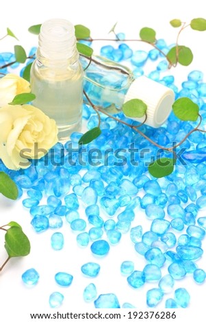 Two bottles of oil and a white rose flanked by a scattering of blue stones.