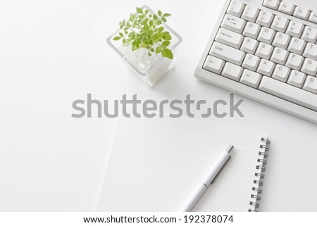 A pen on a notebook sitting by a plant and a computer.
