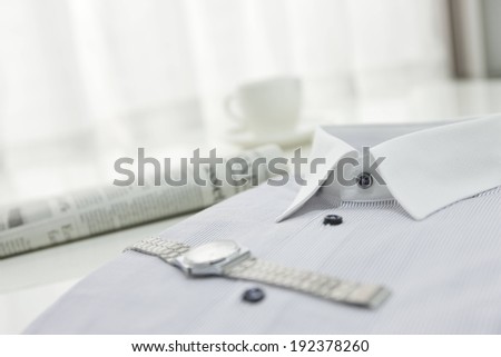 A silver watch on top of a folded shirt.