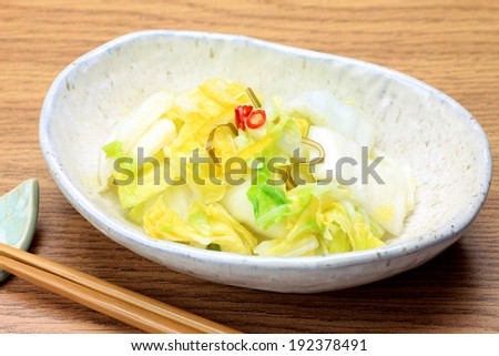 A salad in a white serving dish with chopsticks on a leaf.