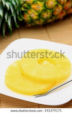 Two slices of pineapple laying on a white square with a whole pineapple in the background.