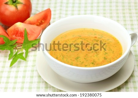 A helping of soup in a white cup with tomatoes on the side.