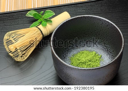 A bamboo whisk beside a bowl with a small amount of green powder in the bottom.