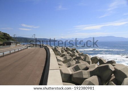 A paved road separated from the ocean by rocks under a blue sky.