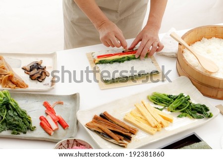 Someone making sushi rolls using rice, meat, and vegetables.