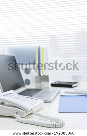 The top of a desk with a telephone, computer, and notebook.