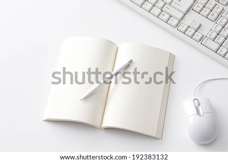 An open blank book with a pen beside a keyboard and mouse.