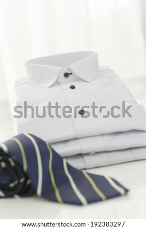 A stack of white business shirts and a rolled tie.