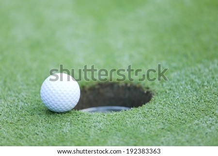 A golf ball on the brink of falling into the hole.