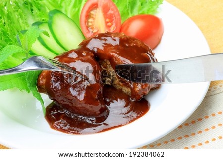 A fork and knife being used to cut into a gravy covered piece of meat.