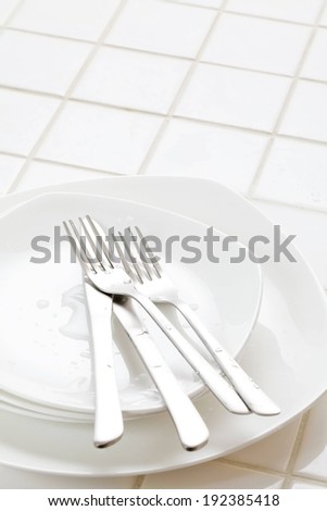 Knives and forks on a small plate that sits on other plates.
