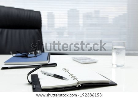 A notebook, pen and glass of water on an office desk.