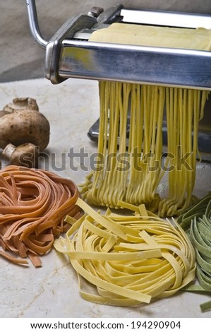 A pasta maker making different color pasta and some mushrooms.