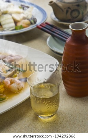 Two plates of food with a yellow drink, teapot and chopsticks.