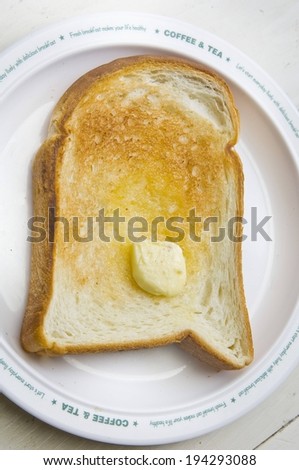 A piece of toasted bread with butter on a white plate.
