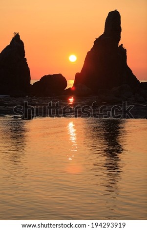 Rock outcroppings in a body of water with the sun in background.