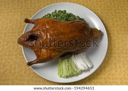 A white plate containing a well roasted bird, laid on a bedding of green vegetable.