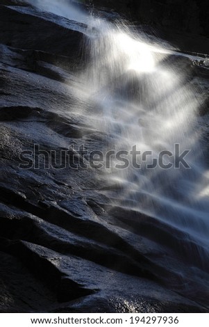 Water droplets splashing down a dark rock wall.