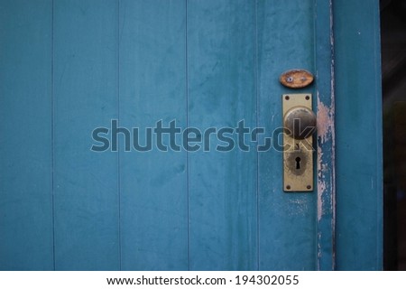 A worn blue wooden door with a brass door knob and paint chips by the knob.