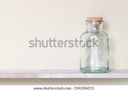 An empty glass jar with a cork lid sitting on a shelf.