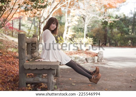 Woman sitting on a bench in the park with fall foliage