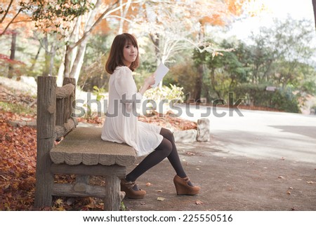 Woman reading on a bench in the park with fall foliage