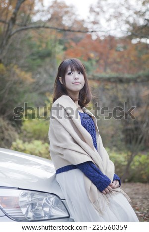 Woman standing in front of the car in the parking lot with autumn leaves