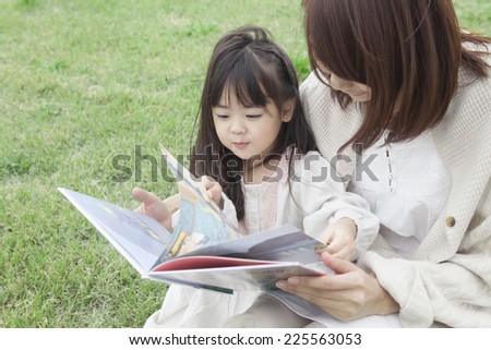 Mother and child reading the picture book on the grass