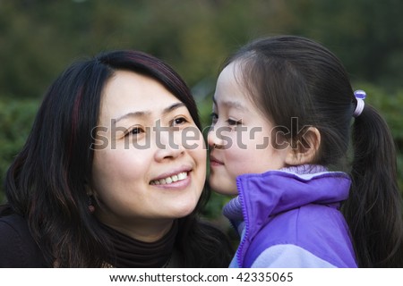 8-year old little asian girl kissing mother in a city park, shanghai, china