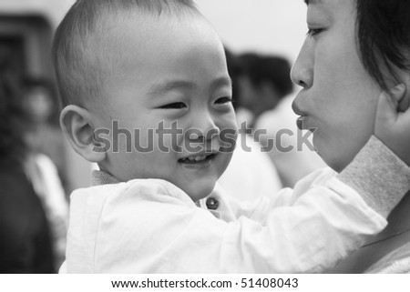 young asian mother kissing her 2-year old son; black and white.