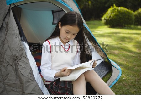 asian schoolgirl sitting in a tent and reading a book