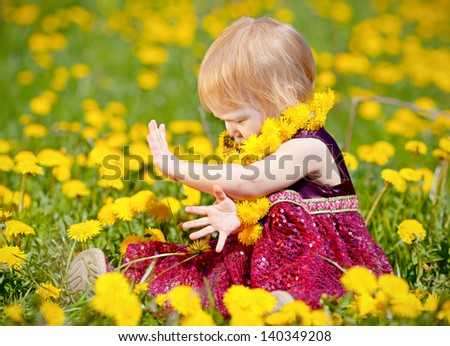 Charming baby sitting in the dandelions. Meadow of yellow dandelions.